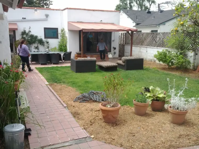 Lush backyard with patio seating, potted plants, and people enjoying the outdoor space.