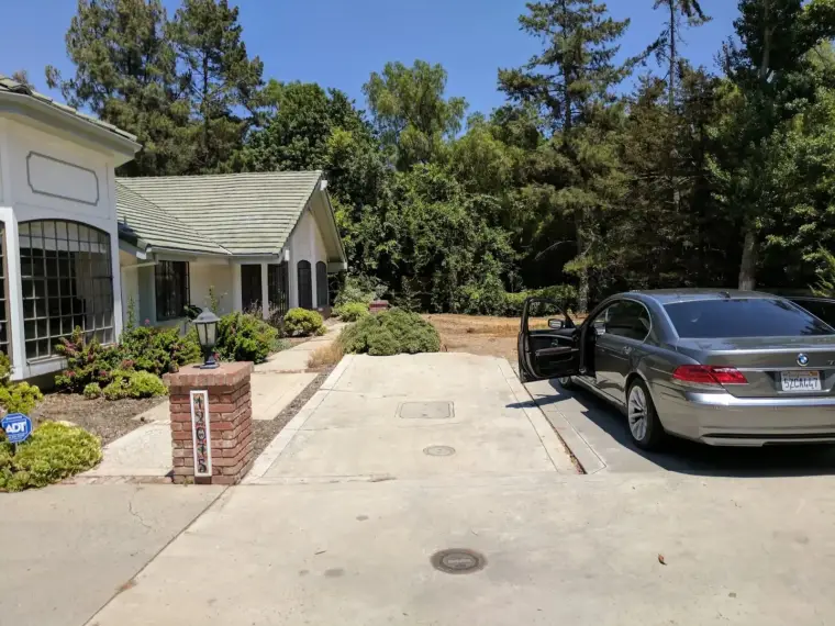 Modern gray car parked in driveway beside a house with a well-manicured front yard.