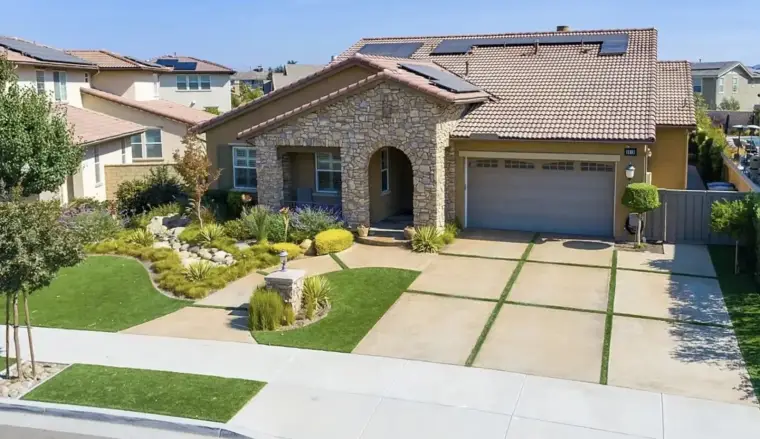 Modern stone-front house with a landscaped yard and solar panels on the roof.