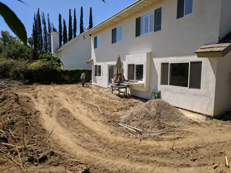 Backyard under construction with dirt, tools, and a person working beside the house.