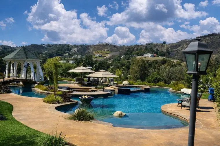 Luxury outdoor pool with gazebo, lounge chairs, and scenic hillside background.