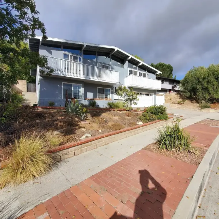 Modern two-story house with balcony, landscaped yard, and brick pathway.