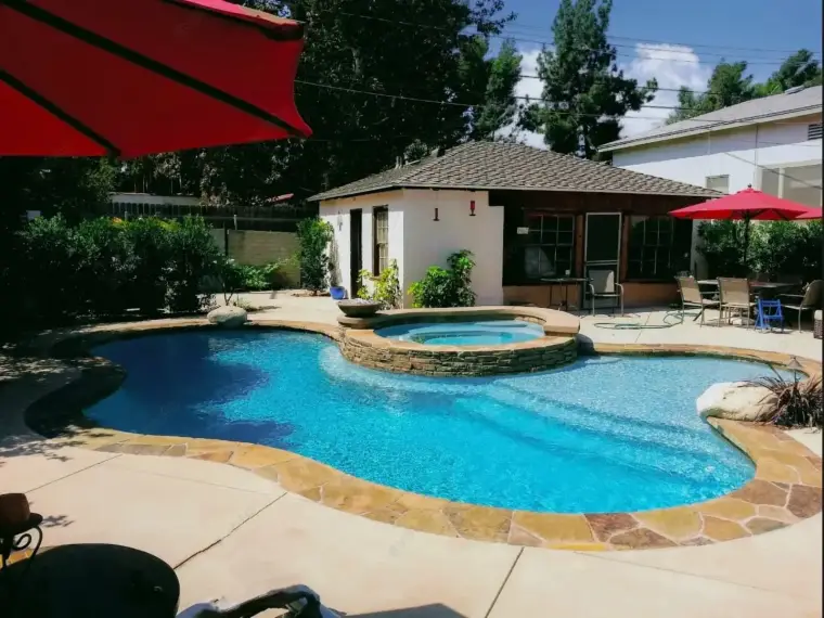 Backyard oasis featuring a sparkling pool, hot tub, and shaded seating area under umbrellas.