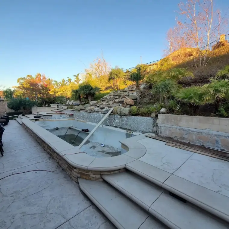 Modern outdoor pool with stone steps, landscaped hillside, and surrounding greenery.
