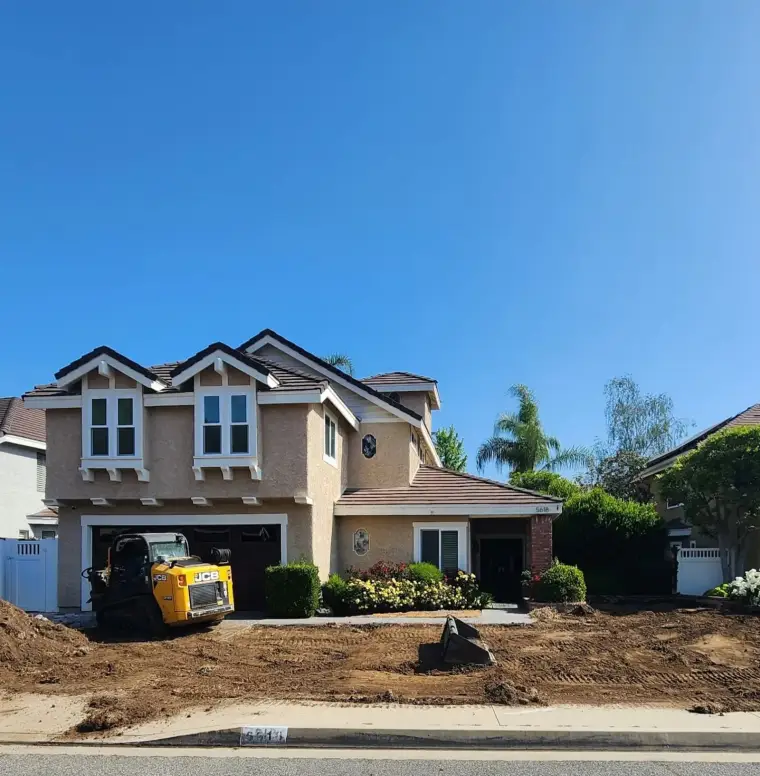 Two-story house with landscaping work, featuring a JCB loader in the yard.