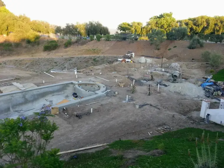 Construction site of an unfinished swimming pool with excavation and equipment visible.