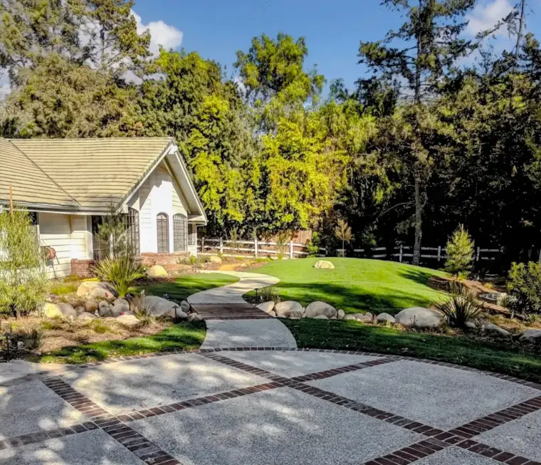 Charming house with landscaped yard, curved pathway, and wooden fence under blue sky.