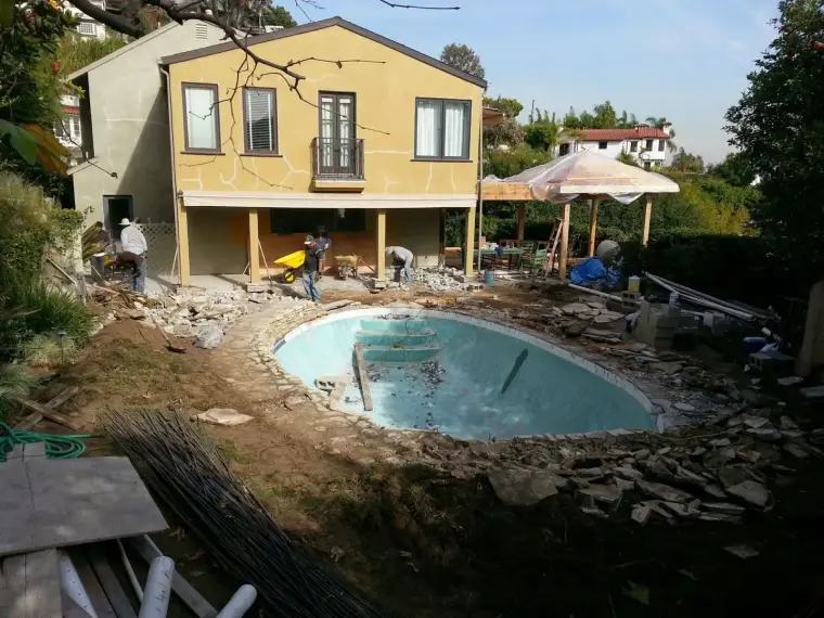 Construction site with unfinished swimming pool and home renovation in a residential backyard.