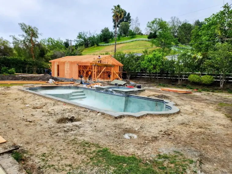 Construction site featuring a wooden frame building and an unfinished swimming pool.