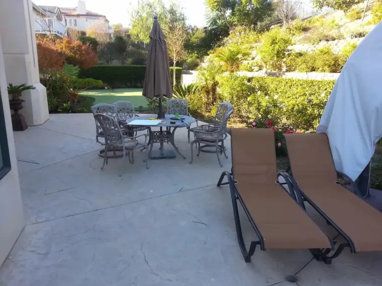 Outdoor patio with a dining table, chairs, and lounge chairs surrounded by greenery.