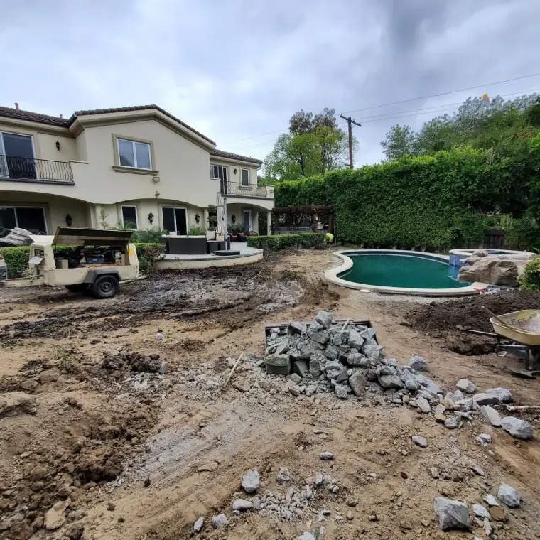 Backyard under renovation with a pool, construction equipment, and scattered rocks.