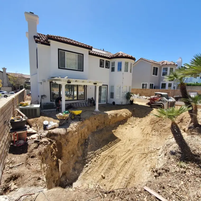 Home undergoing construction with deep excavation in backyard, clear blue sky above.