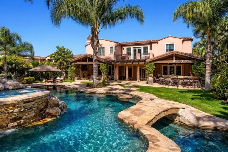 Luxury home with pool, lush landscaping, and outdoor dining area under blue sky.