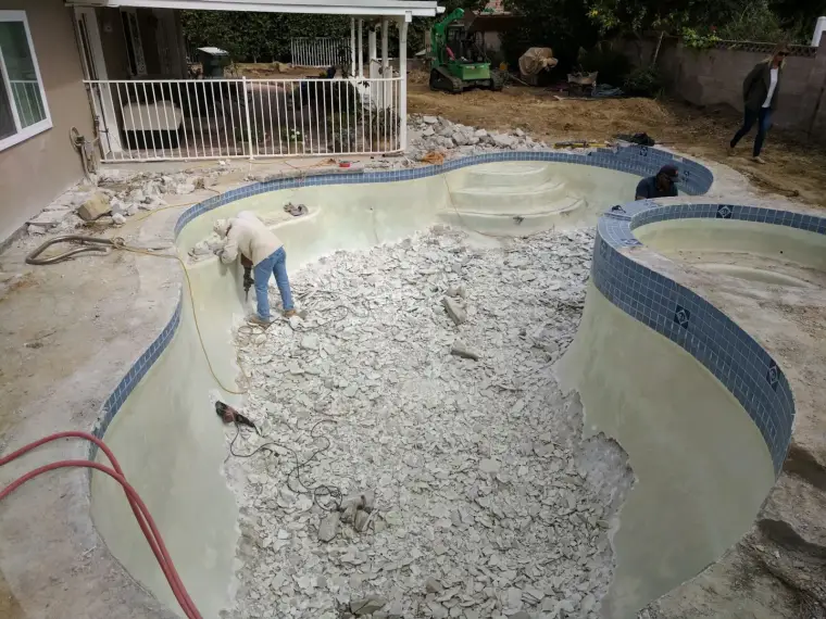 Workers renovating a backyard pool, removing debris and preparing for repairs.
