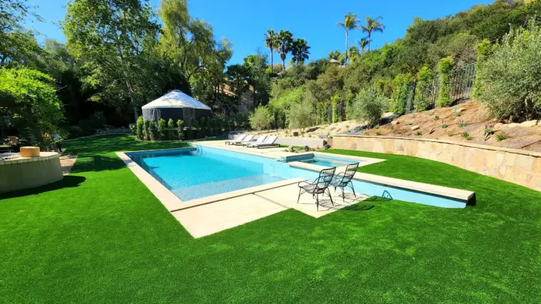 Modern backyard with a sparkling pool, lounge chairs, and lush green landscaping.