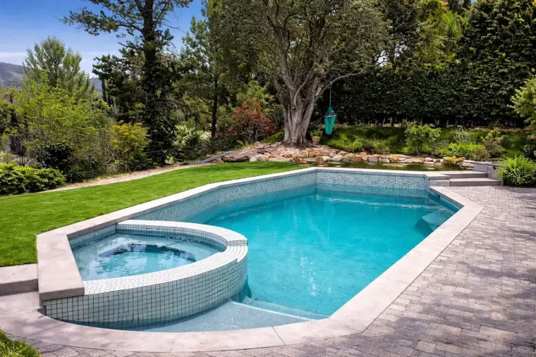 Modern backyard with an elegant swimming pool and jacuzzi, surrounded by lush greenery.