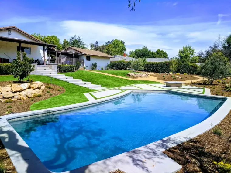 Modern backyard pool with landscaped garden, steps, and lush greenery under a blue sky.