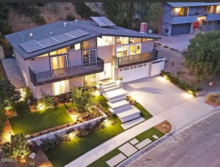 Modern home with solar panels, landscaped yard, and illuminated pathway at dusk.