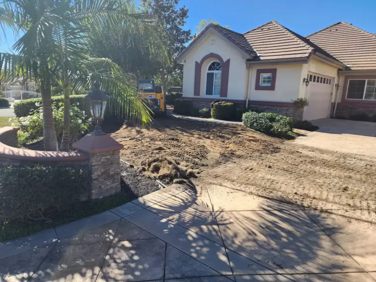 Landscaping project in progress at a residential home with freshly turned soil and palm trees.