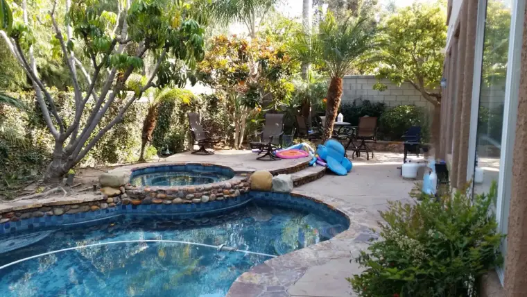 Backyard pool with spa, surrounded by lush greenery and lounge chairs. Relaxing outdoor space.