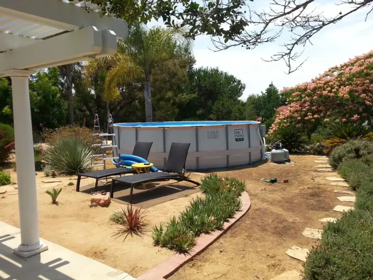 Above-ground pool in a landscaped yard with lounge chairs and flowering shrubs.