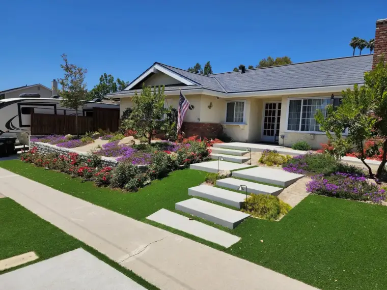 Beautiful landscaped front yard with colorful flowers, green turf, and steps leading to a house.