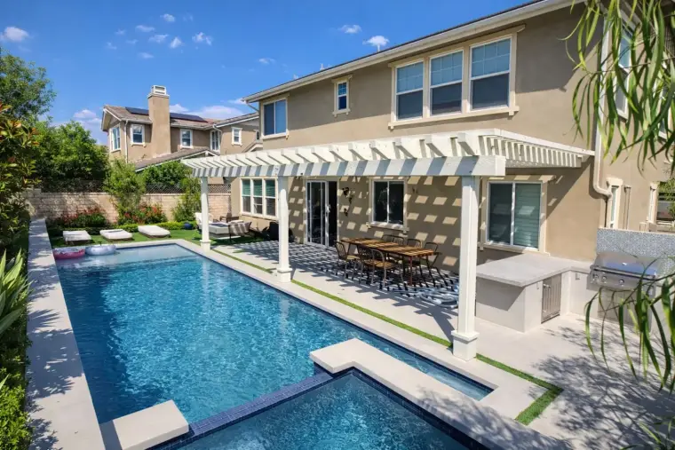Modern home with pool, outdoor dining area, and lush landscaping under a clear blue sky.