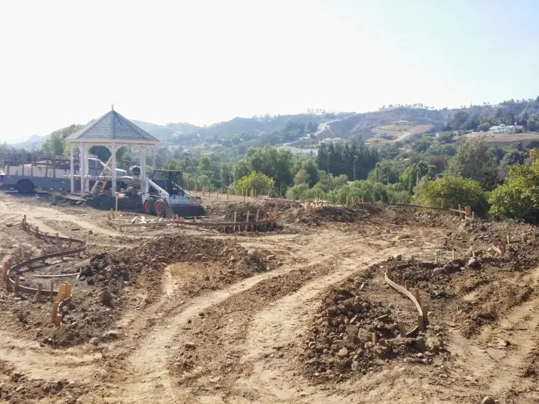 Construction site with curved pathways and gazebo amidst hills and trees.