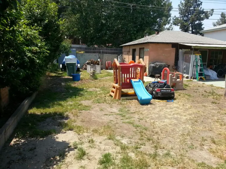Playground set with slide and playhouse in a residential backyard with overgrown grass.