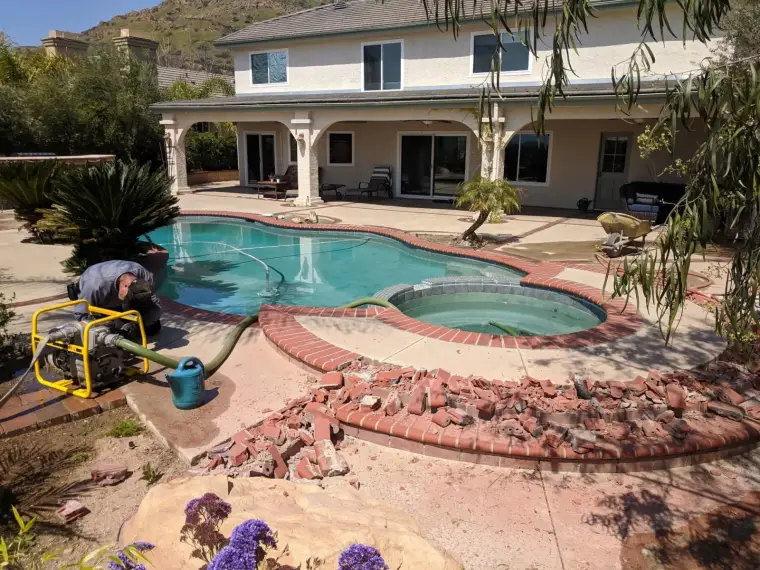 Worker repairing a brick pool edge in a residential backyard with a clear blue pool.