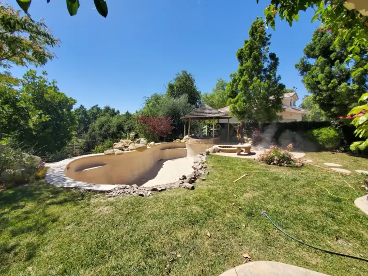 Backyard renovation with a pool, gazebo, and lush landscaping on a sunny day.