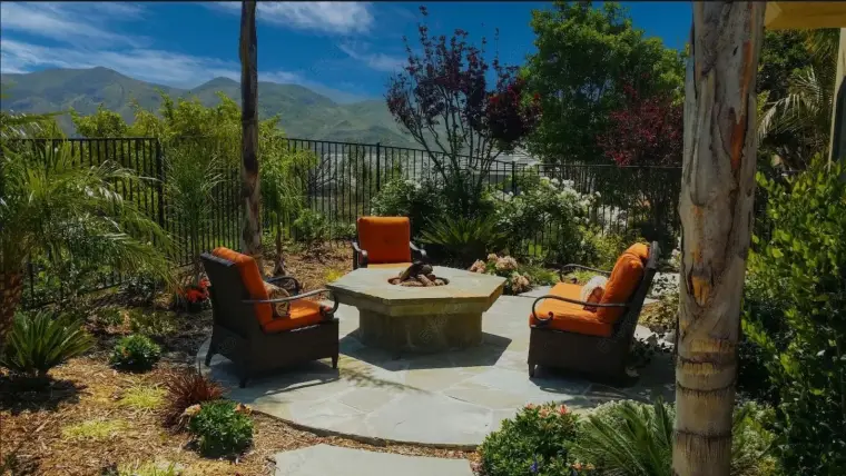 Cozy outdoor seating area with orange chairs, stone fire pit, and lush greenery in the background.