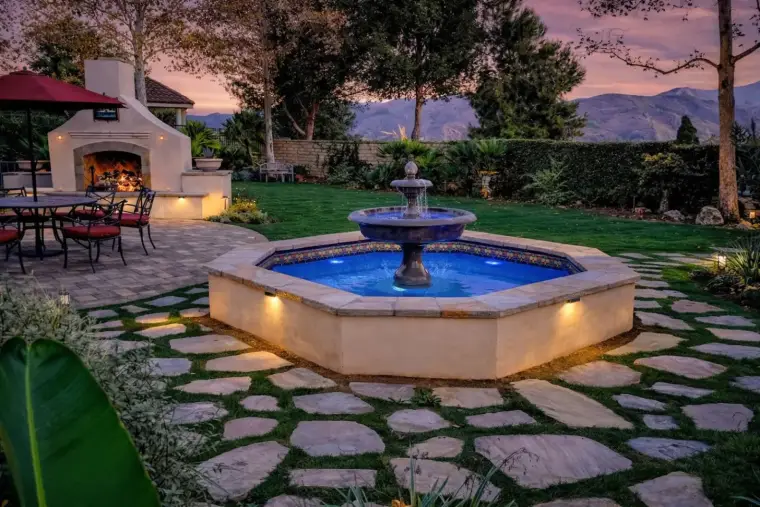 Serene backyard with a fountain, seating area, and sunset backdrop in a landscaped garden.