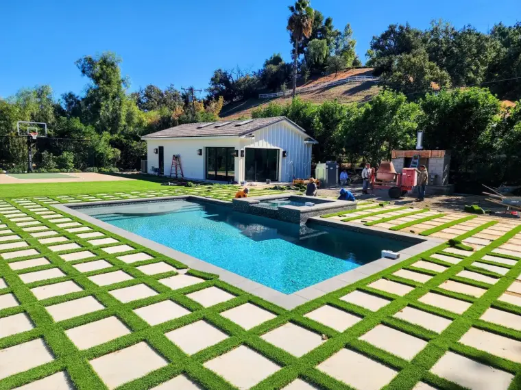 Modern backyard with a swimming pool, patio, and landscaped grass area under a clear blue sky.