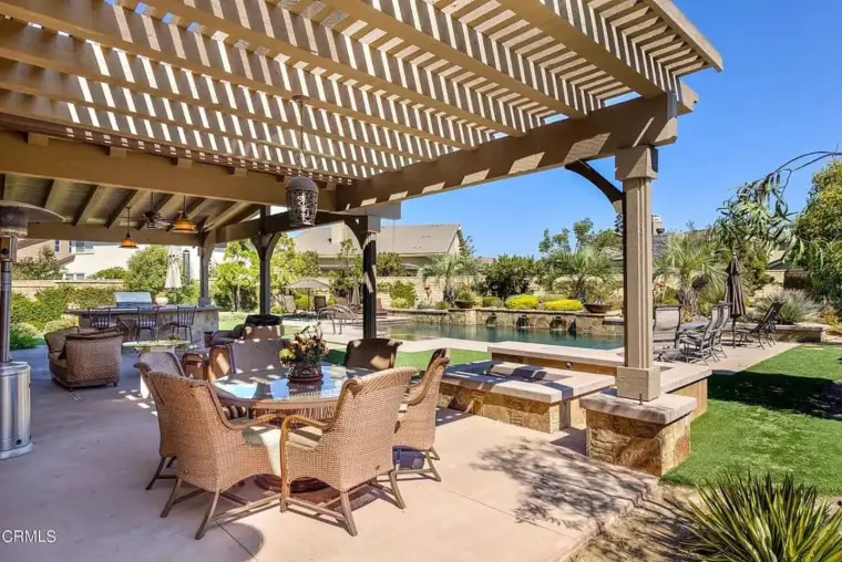 Outdoor patio with seating, pool, and landscaped garden under a pergola.