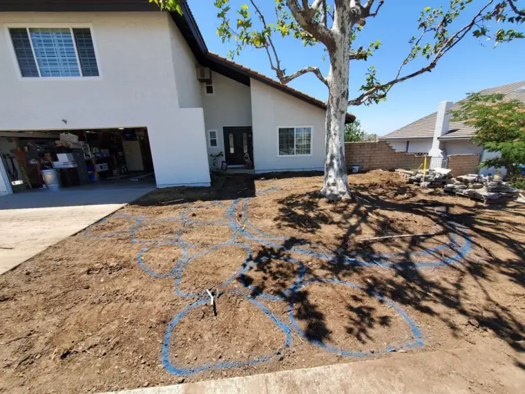 Front yard landscaping project with outlined garden beds around a tree and a garage.