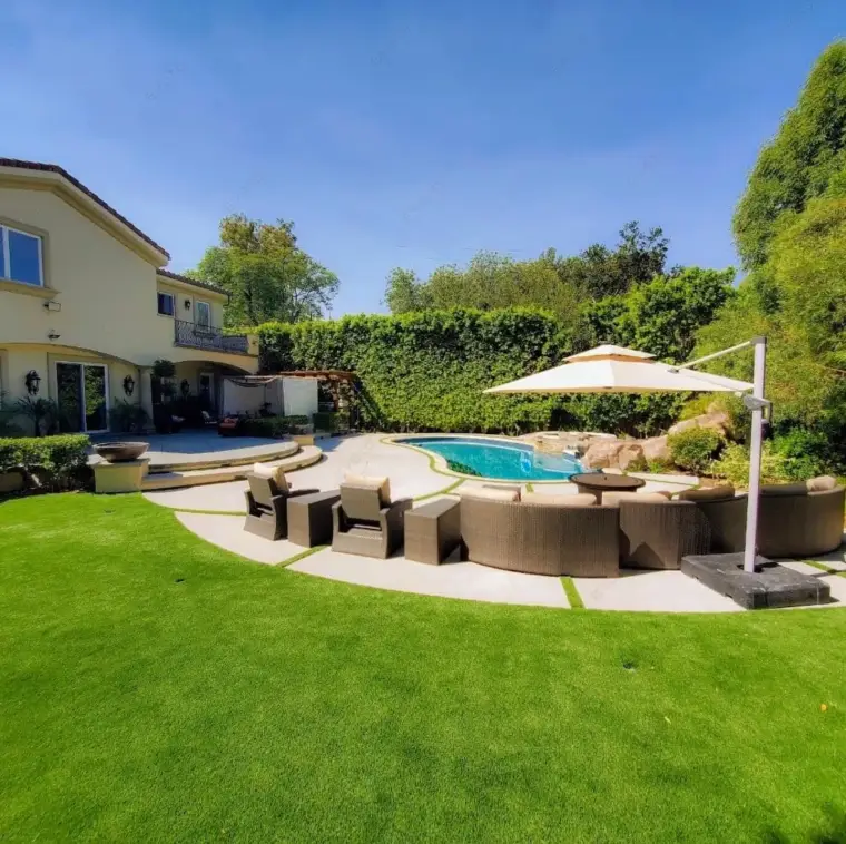 Modern backyard with a pool, lounge chairs, and lush greenery under a blue sky.