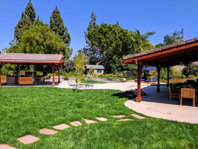 Lush backyard with green lawn, two gazebos, and a pool surrounded by trees and landscaping.