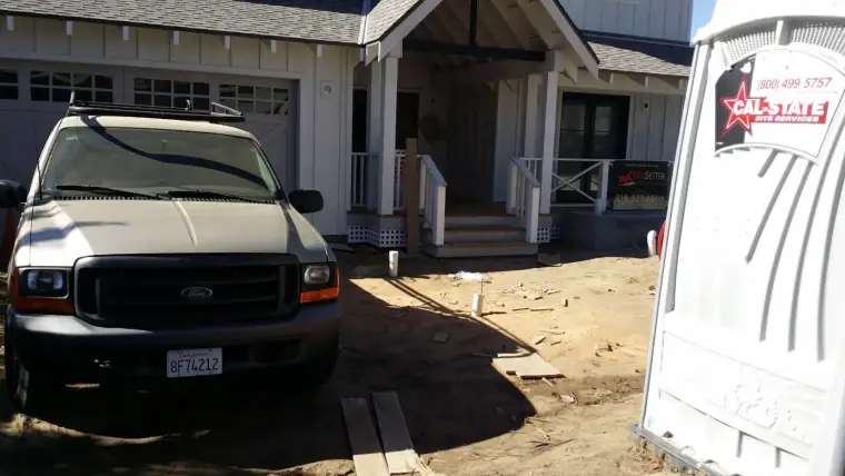 Ford truck parked in front of a house under construction with a portable restroom nearby.
