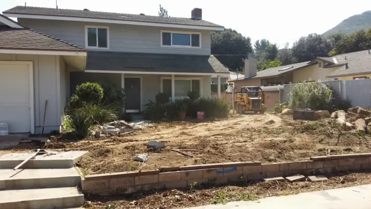 Home renovation with a cleared landscape, stonework, and landscaping equipment in front yard.