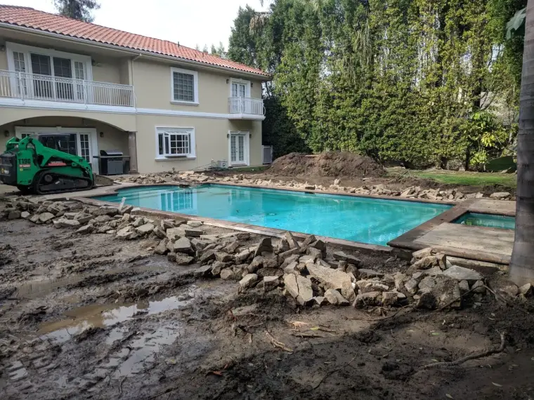 Home backyard pool construction with landscaping and machinery near a house.