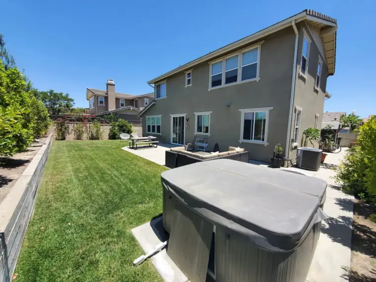 Backyard view of a modern home featuring a hot tub, patio, and well-maintained lawn.