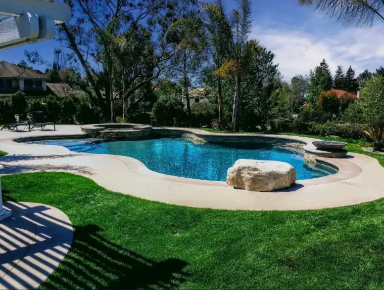 Luxurious backyard with a sparkling swimming pool, rock features, and lush greenery.