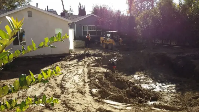 Construction site with excavation equipment and a worker next to a house.