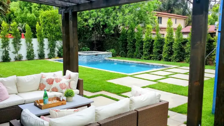 Cozy outdoor seating area with a pool and lush green landscaping in a sunny backyard.