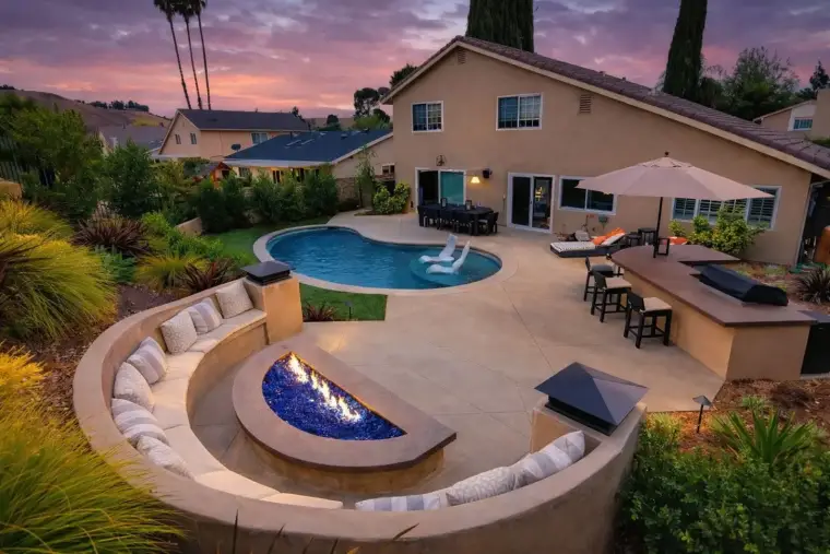 Backyard oasis with pool, fire pit, and outdoor seating at sunset, surrounded by lush landscaping.