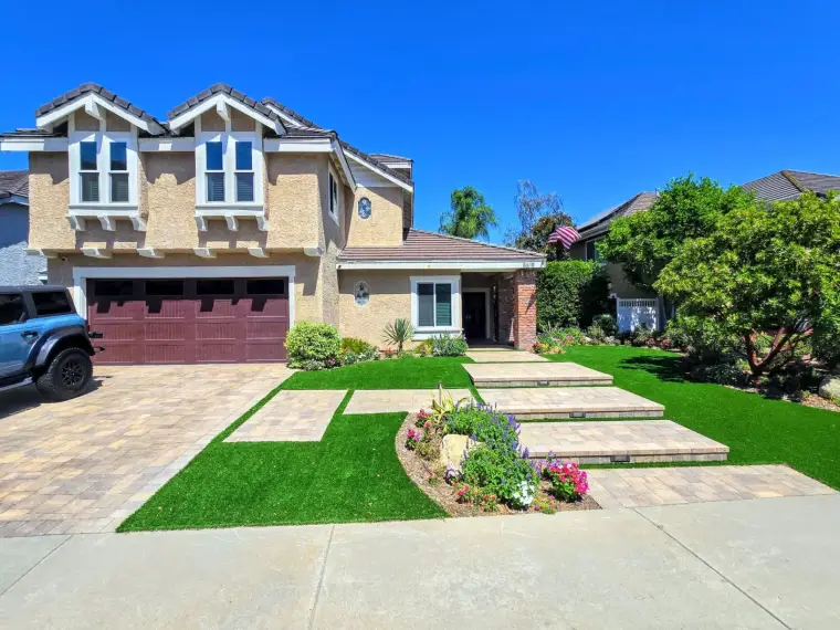 Modern two-story house with landscaped yard, paver driveway, and vibrant flower beds.