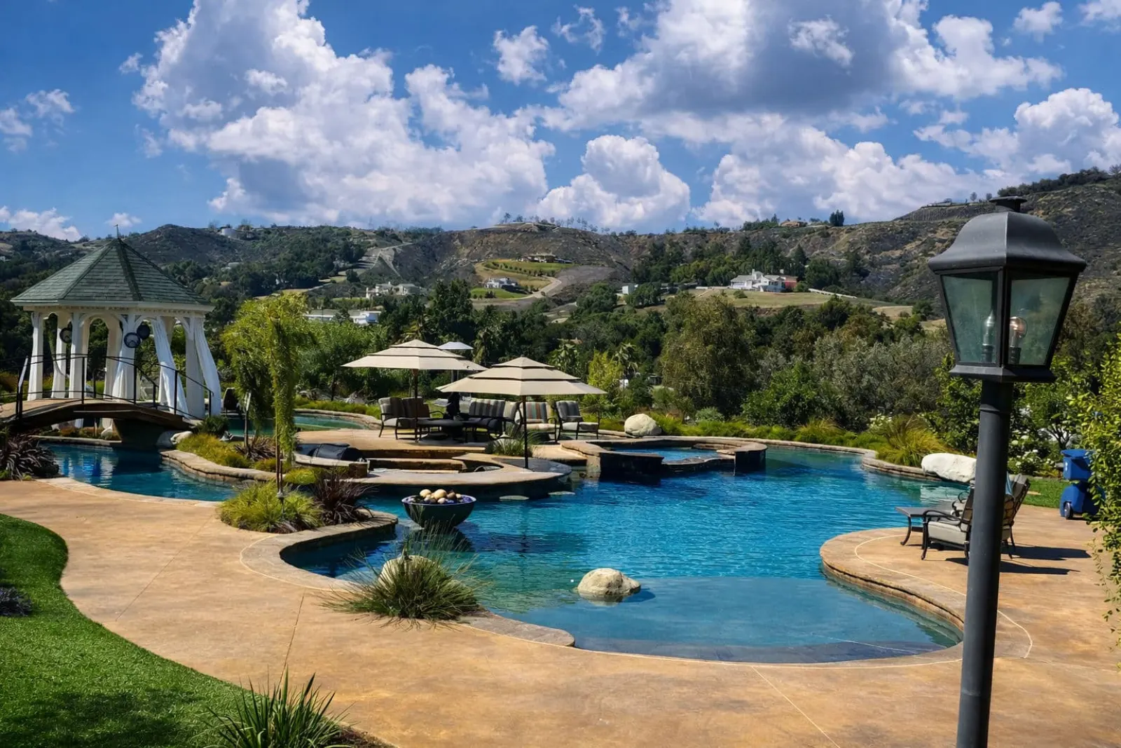 Luxury outdoor pool with gazebo, lounge chairs, and scenic hillside background.