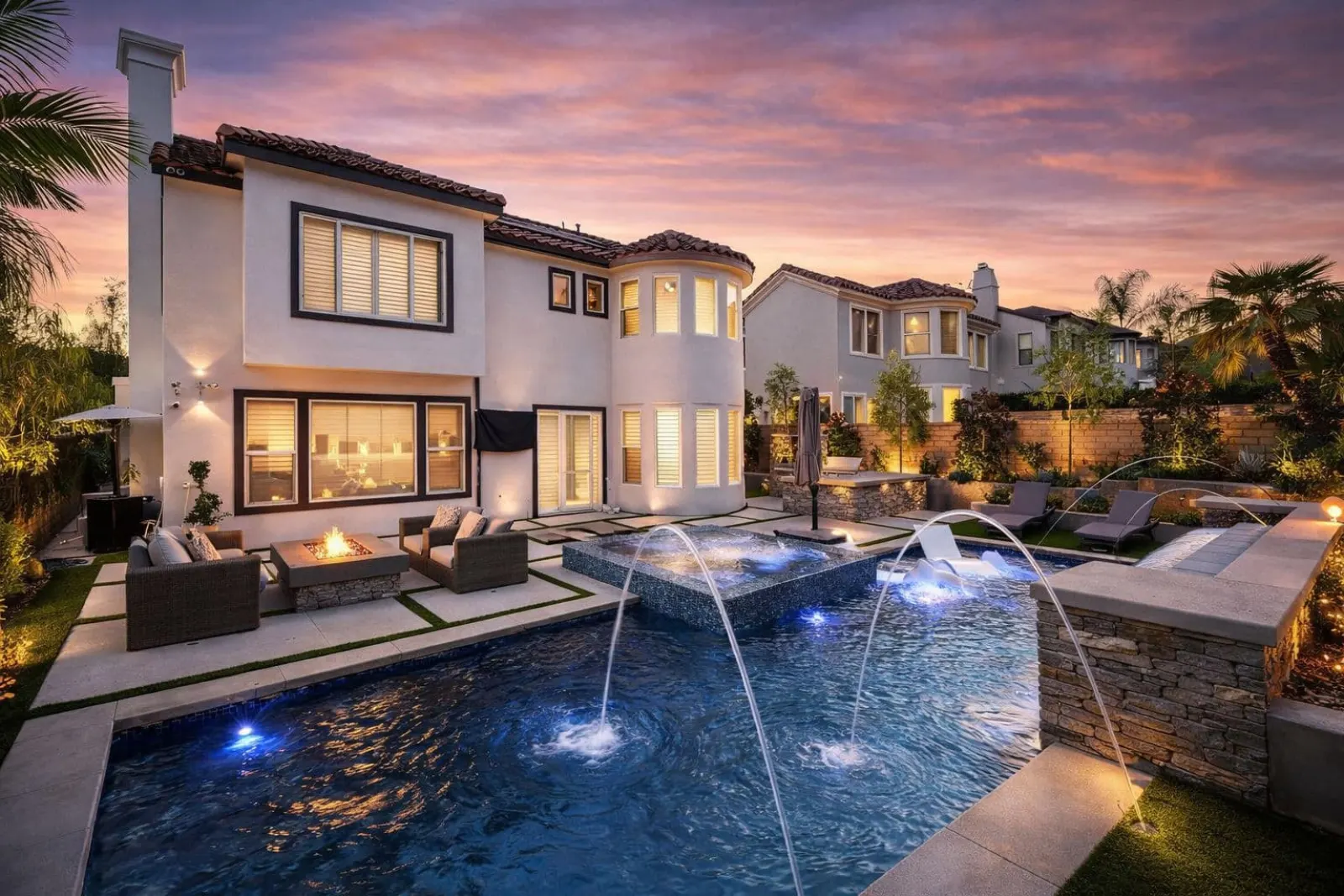 Luxury home exterior at sunset with pool, fountains, and landscaped garden.
