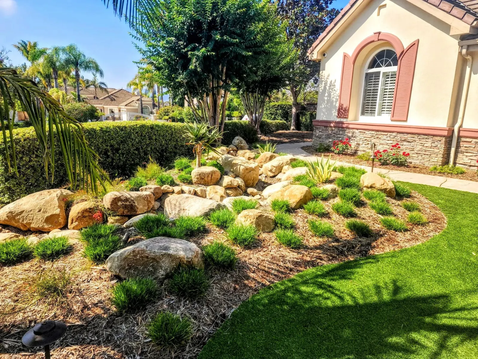 Lush landscaped garden with rocks, greenery, and a decorative pond by a suburban home.